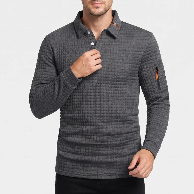 Man wearing a dark grey, waffle-knit long-sleeve polo shirt with two white buttons and an orange zippered sleeve pocket.