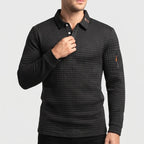 Man wearing a black, quilted long-sleeve polo with white buttons, a tan collar trim, and an orange sleeve accent, adjusting the collar.