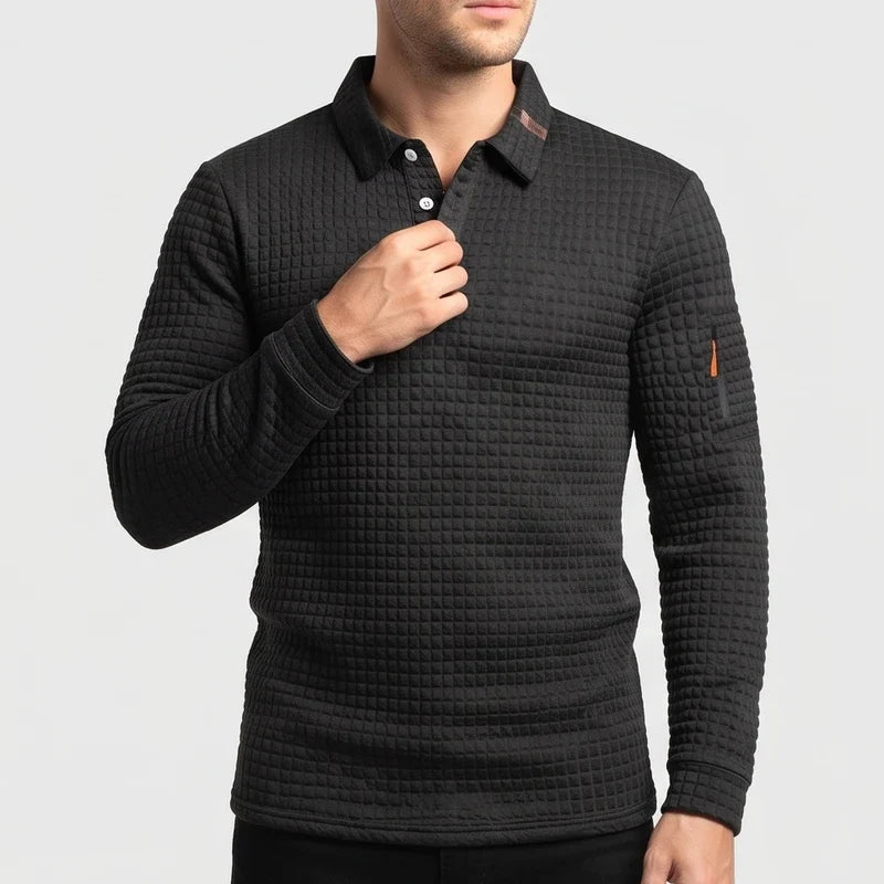 Man wearing a black, quilted long-sleeve polo with white buttons, a tan collar trim, and an orange sleeve accent, adjusting the collar.