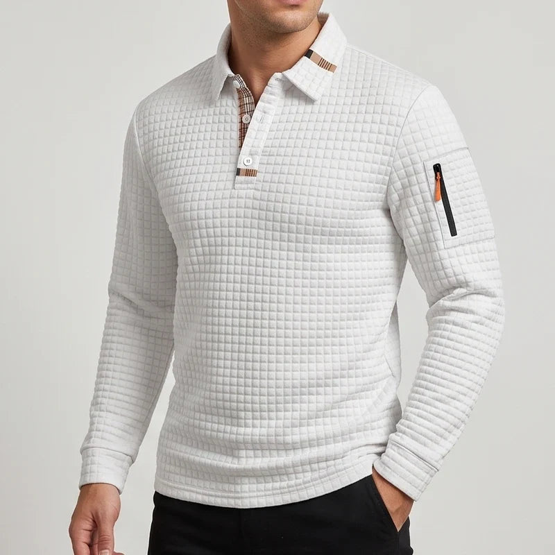 Man wearing a light gray quilted long-sleeve polo shirt with a plaid collar lining and a zippered pocket on the left sleeve.