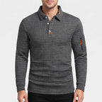 Man wearing a dark grey long sleeve polo shirt with a waffle-knit texture and an orange zipper pocket on the sleeve.