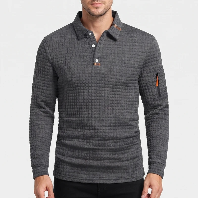 Man wearing a dark grey long sleeve polo shirt with a waffle-knit texture and an orange zipper pocket on the sleeve.
