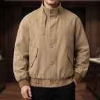 Man wearing a tan jacket with a stand-up collar, button front, side flap pockets, and ribbed cuffs and hem.
