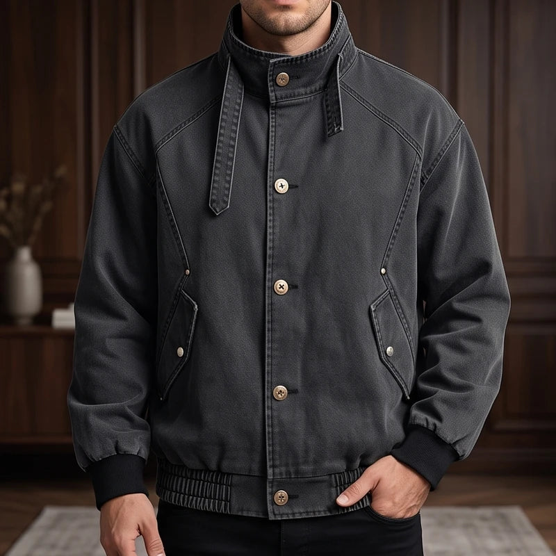 Man wearing a dark grey distressed jacket with a high collar, light buttons, elasticated cuffs, and hem.