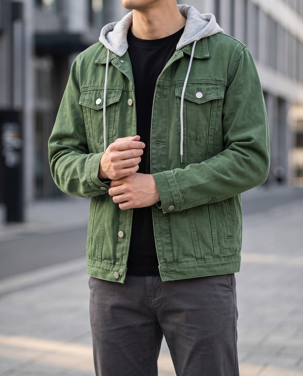 Man wearing a green denim jacket over a black shirt with a gray hooded insert, posing outdoors.