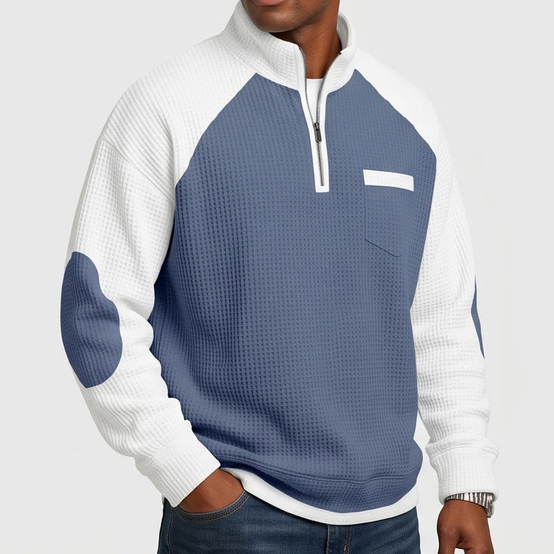 Man wearing a blue and white waffle knit half-zip sweatshirt with a chest pocket and matching elbow patches.