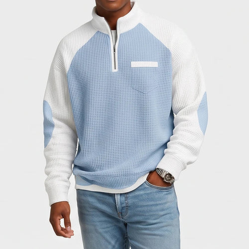 Man wearing a light blue and white color-blocked waffle knit half-zip sweatshirt with a chest pocket and light wash jeans.