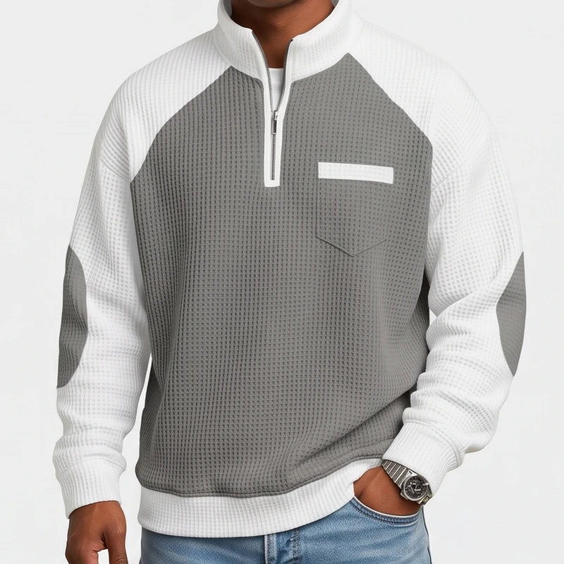 Man wearing a grey and white waffle knit half-zip sweatshirt with a chest pocket and elbow patches.