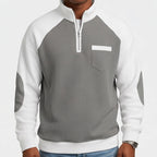 Man wearing a grey waffle knit half-zip sweatshirt with white raglan sleeves and elbow patches.