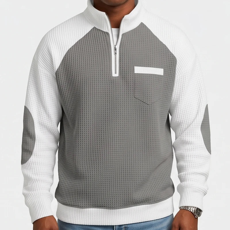 Man wearing a grey waffle knit half-zip sweatshirt with white raglan sleeves and elbow patches.