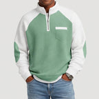 Man wearing a green and white color block waffle knit half-zip sweatshirt with a chest pocket and elbow patches.