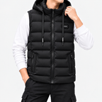 Man wearing a black hooded puffer vest with a full zipper, drawstring pulls, and zippered pockets over a white long-sleeve shirt.