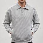 Man wearing a light gray long-sleeve polo sweatshirt with a textured diagonal rib pattern, hands in front pockets.