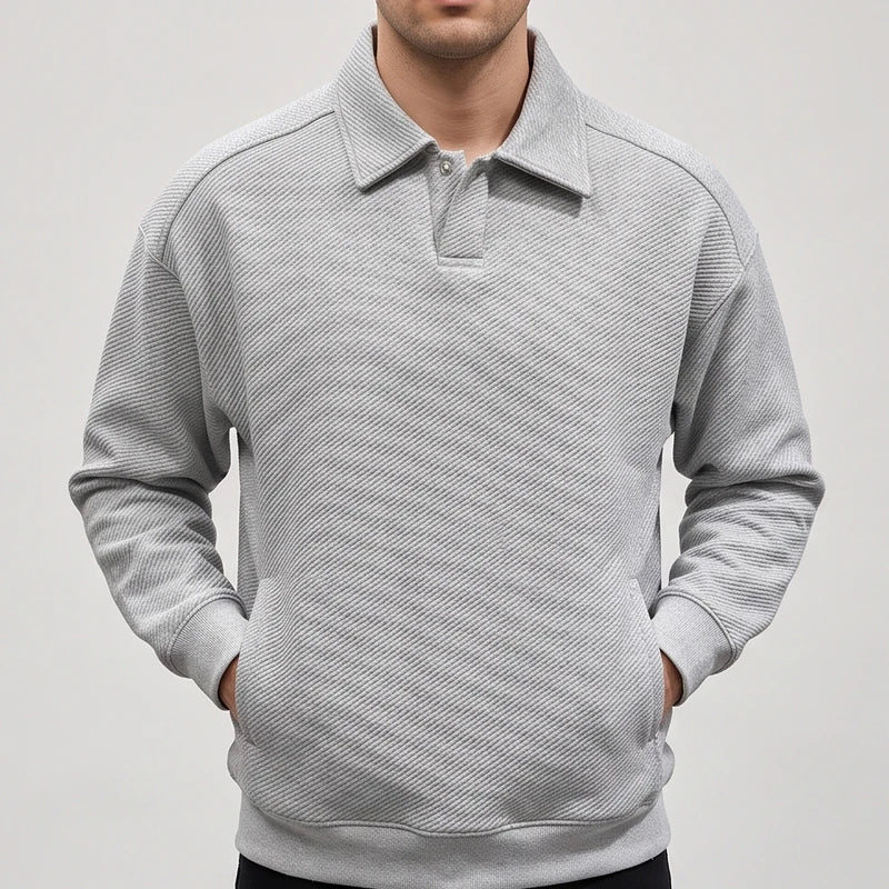 Man wearing a light gray long-sleeve polo sweatshirt with a textured diagonal rib pattern, hands in front pockets.