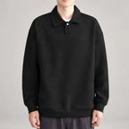 Man wearing a black long-sleeve polo sweatshirt with a textured diagonal pattern and a single white button collar.