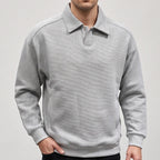 Man wearing a light gray long-sleeve polo sweatshirt with a textured diagonal rib pattern, posed with one hand in pocket.
