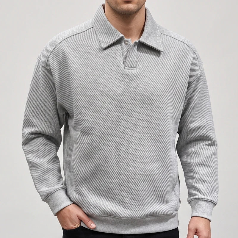 Man wearing a light gray long-sleeve polo sweatshirt with a textured diagonal rib pattern, posed with one hand in pocket.