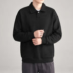 Man wearing a black long-sleeve polo shirt with a subtle diagonal textured pattern and a single white button placket.