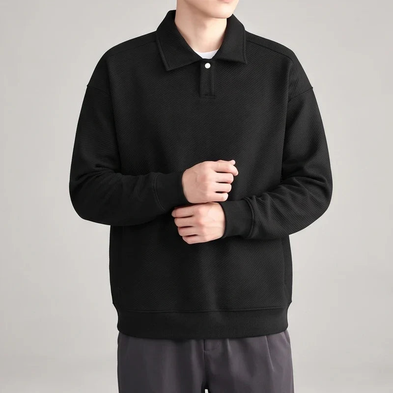 Man wearing a black long-sleeve polo shirt with a subtle diagonal textured pattern and a single white button placket.