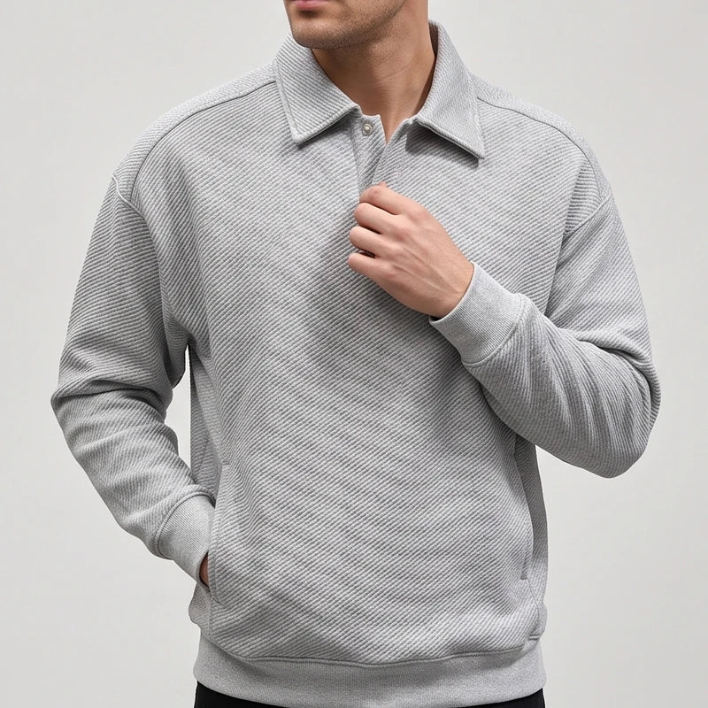 Man wearing a light gray long-sleeve collared sweatshirt with a diagonal ribbed texture and a two-button placket, hand in pocket.