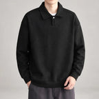 Man wearing a black long-sleeve polo sweatshirt with a textured diagonal stripe pattern and single white button closure.