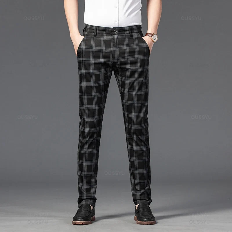 Man wearing black and gray plaid straight-leg trousers with a white shirt, hands in pockets, standing on a dark background.