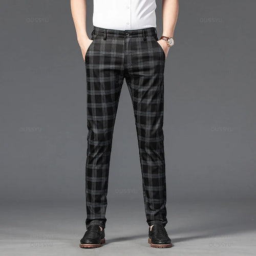 Man wearing black and gray plaid straight-leg trousers with a white shirt, hands in pockets, standing on a dark background.