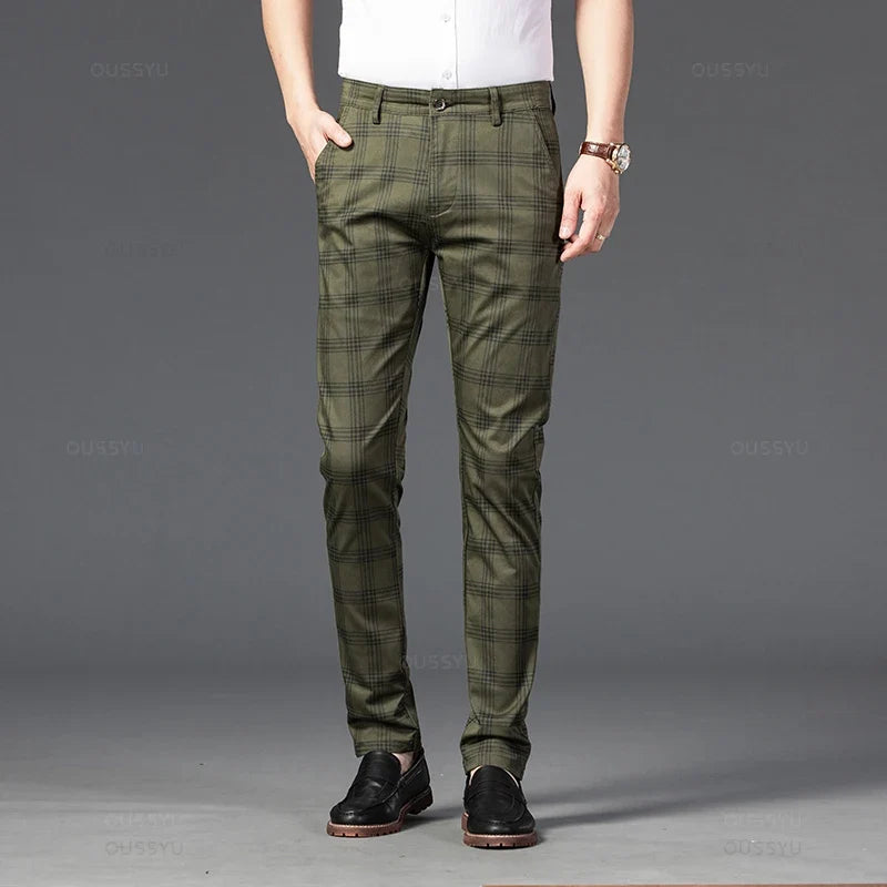 Man wearing olive green plaid straight-leg trousers, a white shirt, and black loafers, standing with one hand in his pocket.