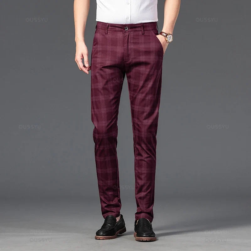 Man wearing burgundy plaid straight-leg trousers with a white shirt and black slip-on shoes, standing with one hand in a pocket.