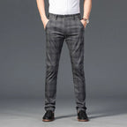 Man wearing dark grey plaid straight-leg trousers with hands in pockets, a white shirt, and black dress shoes.