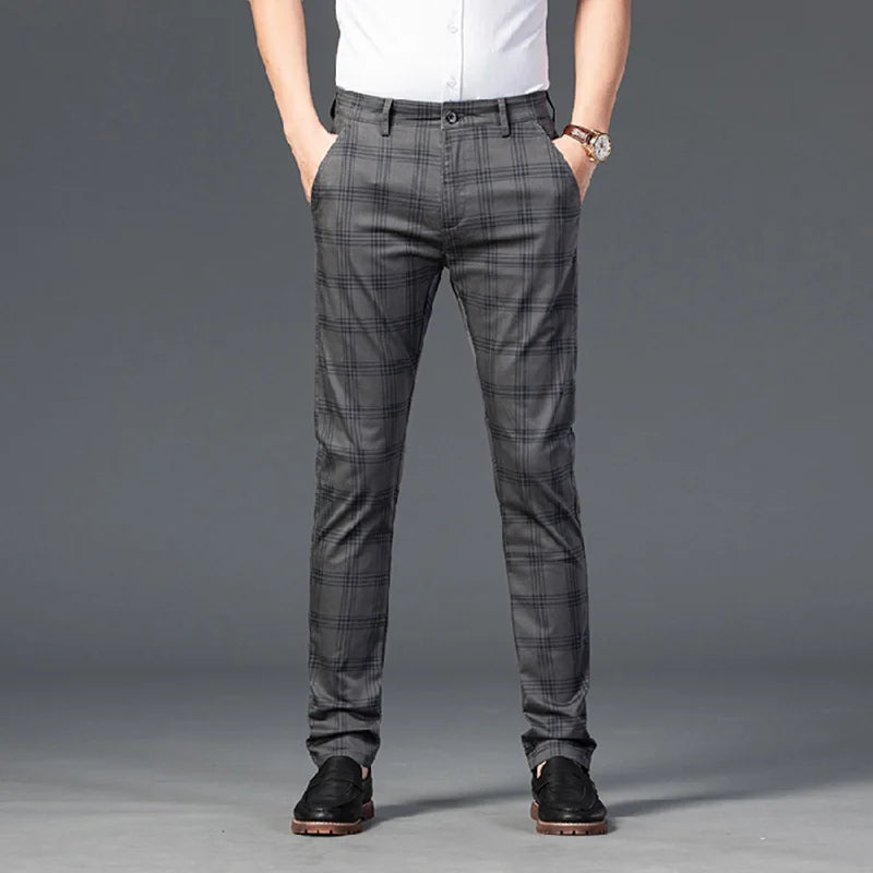 Man wearing dark grey plaid straight-leg trousers with hands in pockets, a white shirt, and black dress shoes.