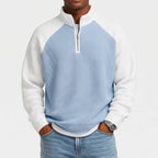 Man wearing a light blue and white color-block waffle knit quarter-zip sweatshirt with raglan sleeves and light wash jeans.