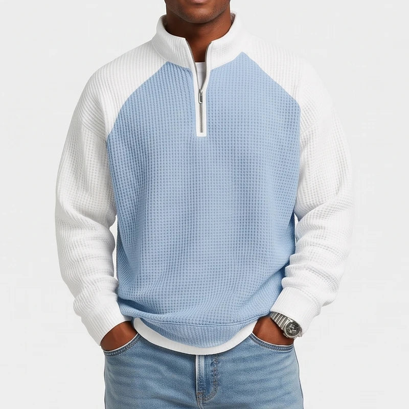 Man wearing a light blue and white color-block waffle knit quarter-zip sweatshirt with raglan sleeves and light wash jeans.