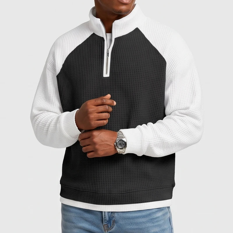 Man wearing a color-block black and white waffle knit quarter-zip sweatshirt with raglan sleeves and a silver zipper.