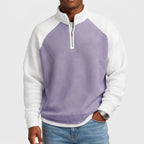 Man wearing a purple and white color-block waffle knit quarter-zip top with light blue jeans and a silver watch.