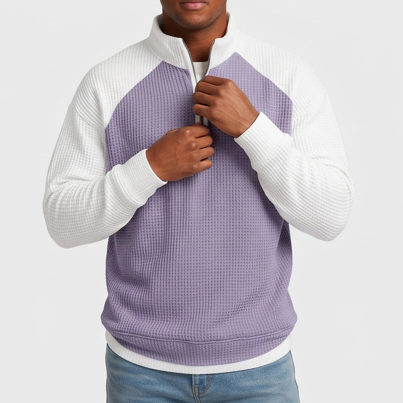 Man wearing a purple and white color-blocked waffle knit quarter-zip, his hands adjusting the zipper.