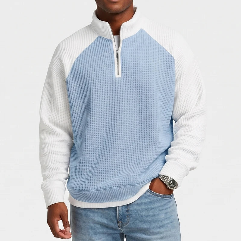 Man wearing a light blue and white waffle knit quarter-zip sweatshirt with raglan sleeves and a metal zipper, hand in pocket.