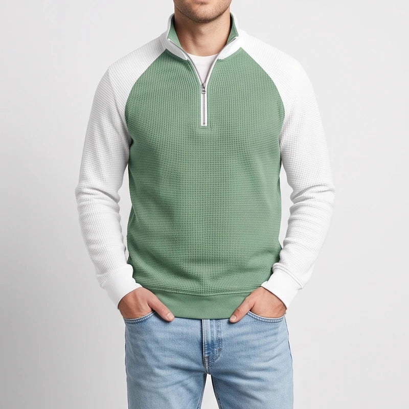 Man wearing a two-tone green and white waffle knit quarter-zip pullover with light blue jeans, hands in pockets.