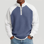 Man wearing a blue and white waffle knit quarter-zip sweatshirt with raglan sleeves and jeans, hands in pockets.