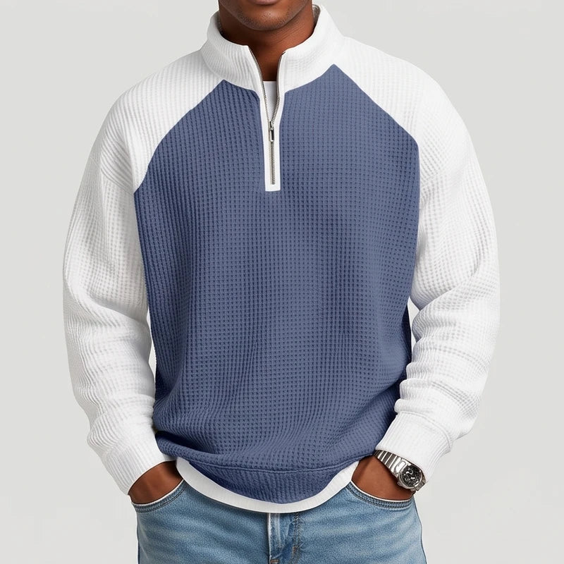 Man wearing a blue and white waffle knit quarter-zip sweatshirt with raglan sleeves and jeans, hands in pockets.