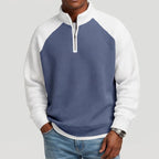 Man wearing a two-toned waffle knit quarter-zip sweatshirt with white sleeves and collar, and a blue body.