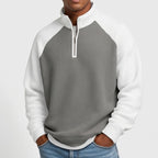 Man wearing a gray waffle-knit quarter-zip sweatshirt with white raglan sleeves and a matching white collar, hands in jeans pockets.