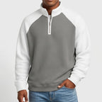 Man wearing a two-tone gray and white waffle knit quarter-zip sweatshirt with raglan sleeves and a white zipper.