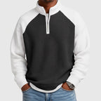 Man wearing a black and white color-block waffle knit quarter-zip sweatshirt with raglan sleeves and a silver zipper, hands in jeans pockets.