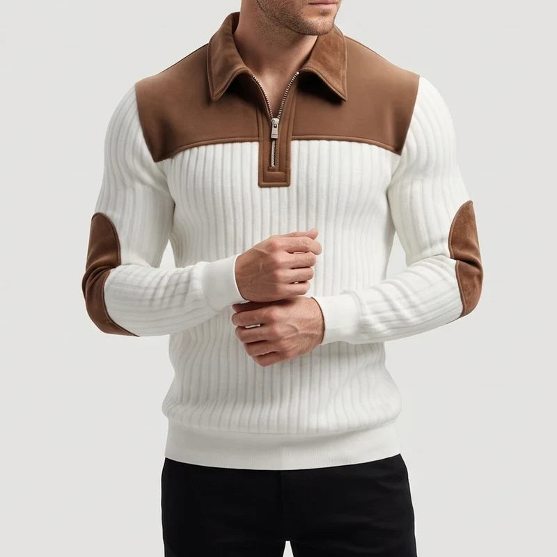Man wearing a white ribbed quarter-zip jumper with brown collar, shoulder panels, and elbow patches, posing with hands clasped.
