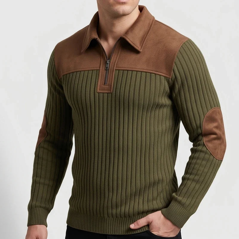 Man wearing a green ribbed knit quarter-zip jumper with brown collar, shoulder, and elbow patches, posing with a hand in his pocket.