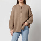 Woman wearing an oversized, ribbed knit, light brown cardigan with gold buttons and light wash jeans.