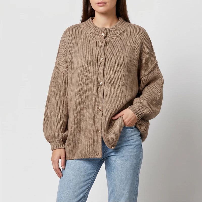 Woman wearing an oversized, ribbed knit, light brown cardigan with gold buttons and light wash jeans.