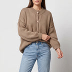 Woman wearing a light brown knit cardigan with golden buttons, an oversized fit, and light wash jeans.