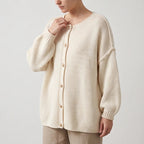 Woman wearing an oversized cream knit cardigan with dropped shoulders, puff sleeves, and gold-rimmed buttons, over tan pants.